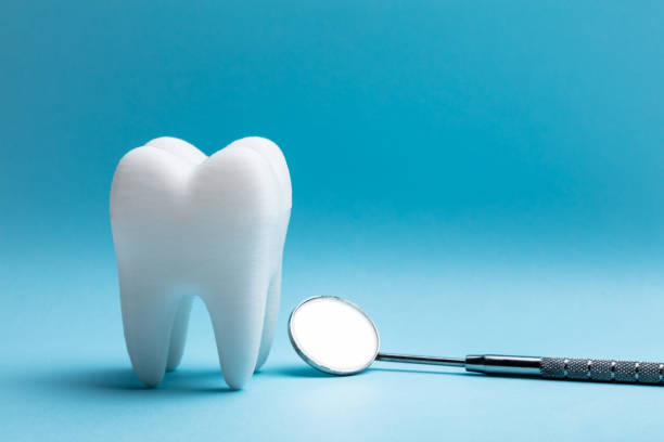 Close-up Of Tooth With Dental Mirror Over Blue Background